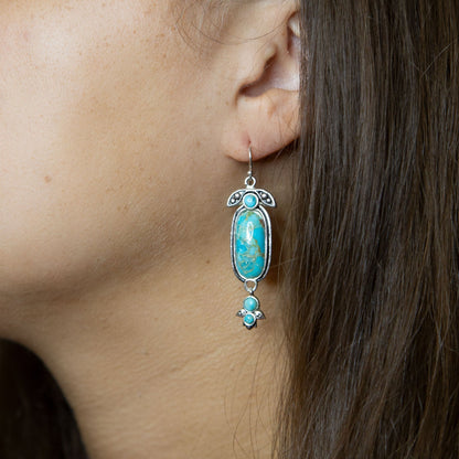 Turquoise earrings worn by a person with dark hair.