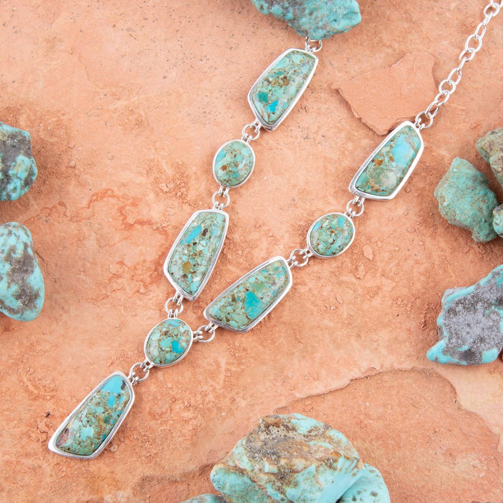 Turquoise necklace with silver chain on a textured surface with turquoise stones.