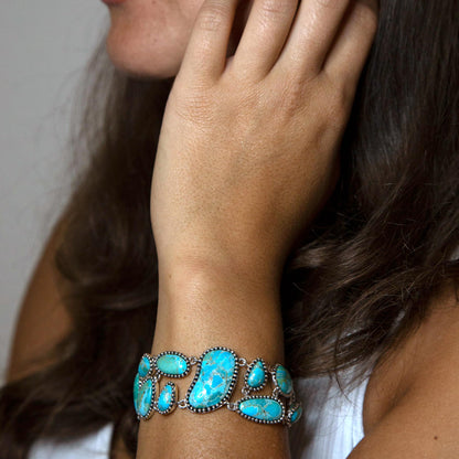 Close-up of a woman's hand wearing a turquoise bracelet with a neutral background