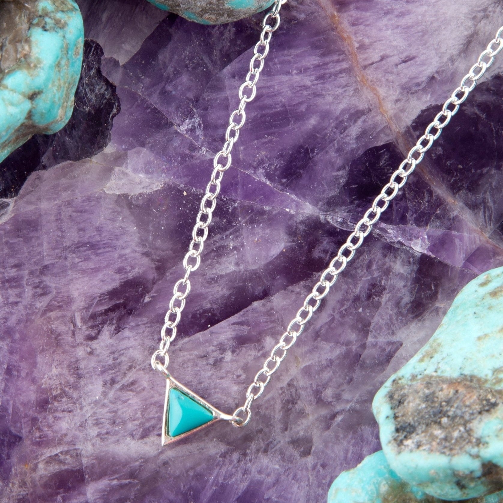 Necklace with a turquoise triangle pendant on a purple crystal background